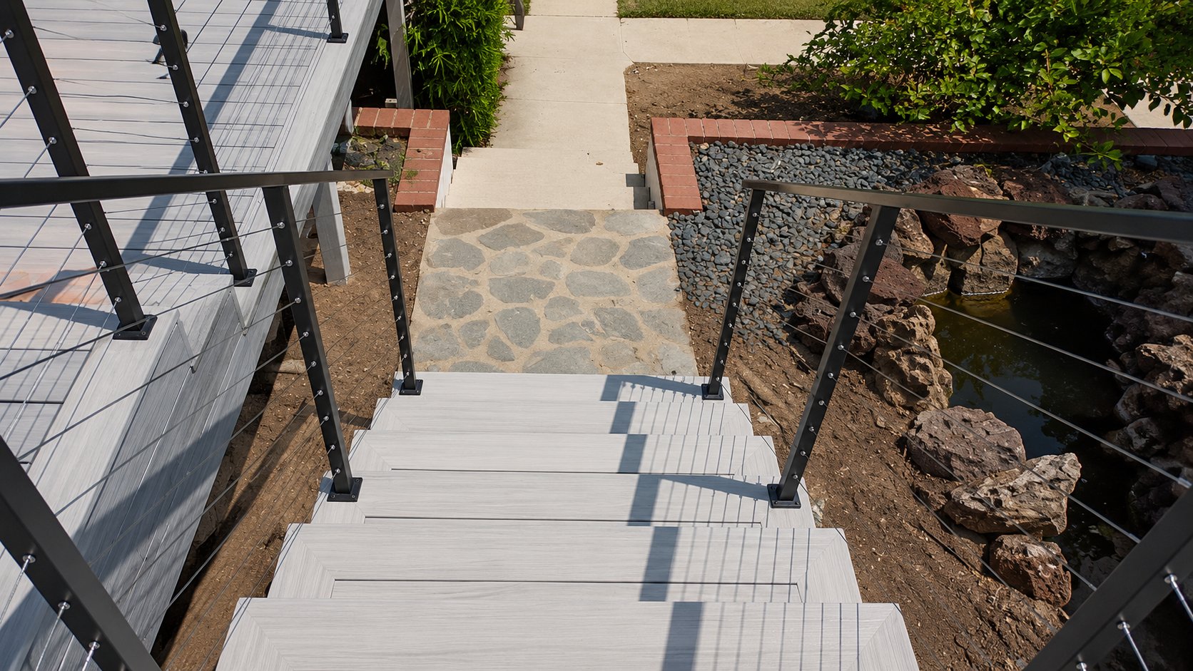 Looking down composite deck stairs framed by stainless cable railing in Los Angeles