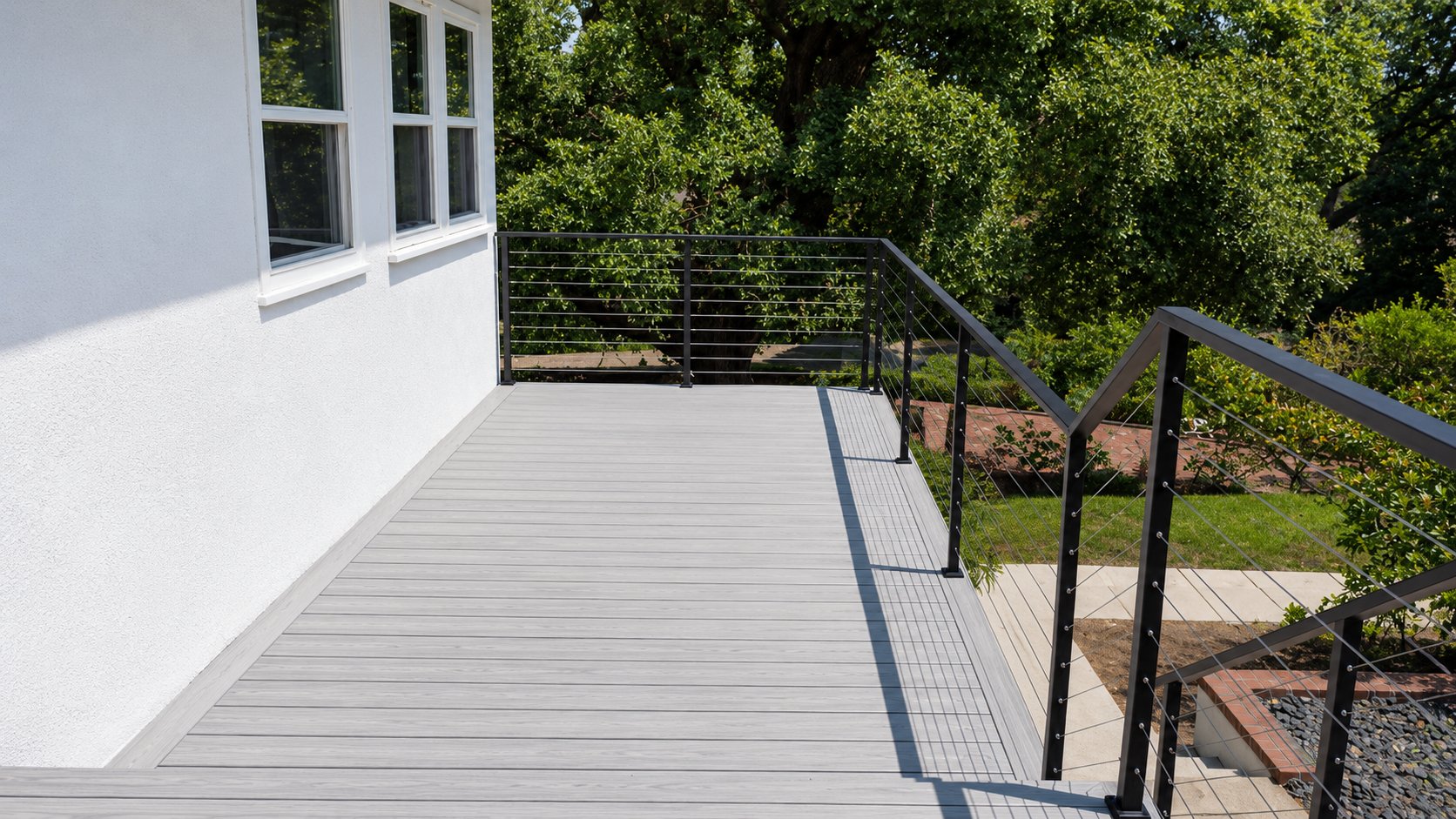 Gray composite deck with stainless cable railing beside a white home in Los Angeles