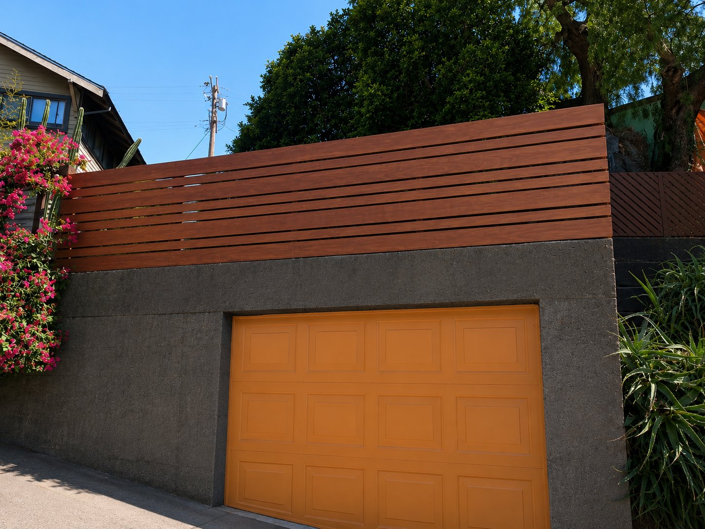 Cedar plank fence above parged concrete retaining wall with raised-panel wood garage door, LA hillside