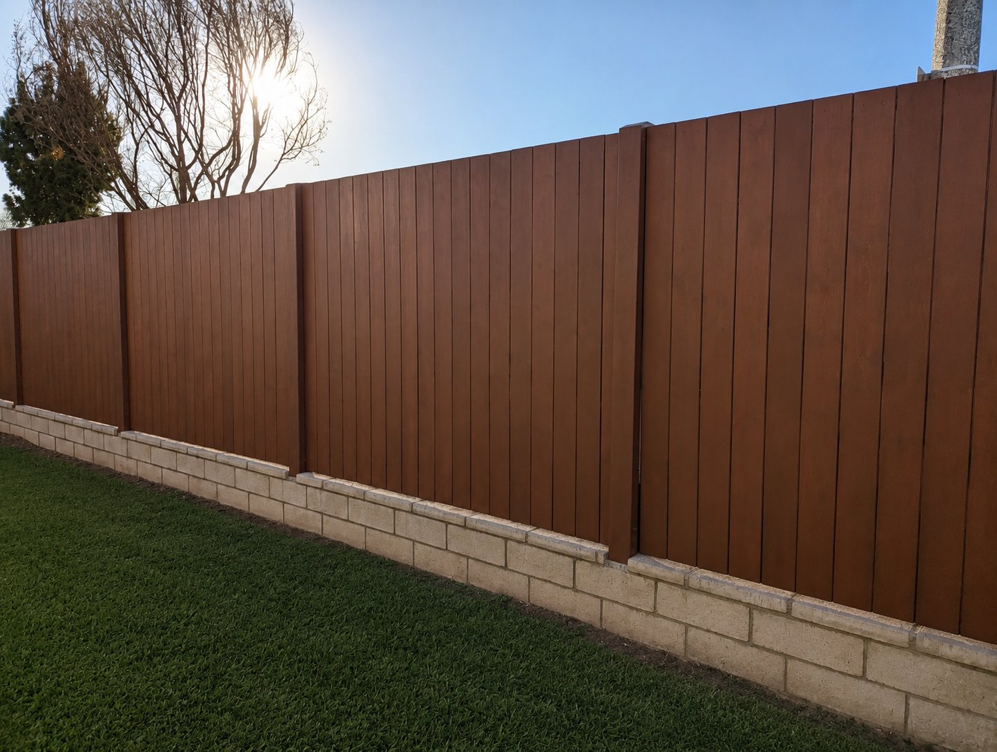 Custom vertical wood privacy fence stained warm reddish-brown, mounted on low concrete block wall in Los Angeles backyard