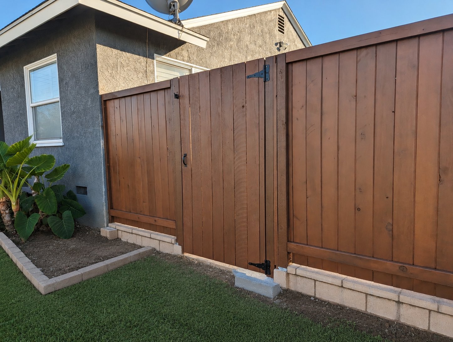 Matching stained wood side gate with black hardware, vertical board pattern, between stucco home and fence run