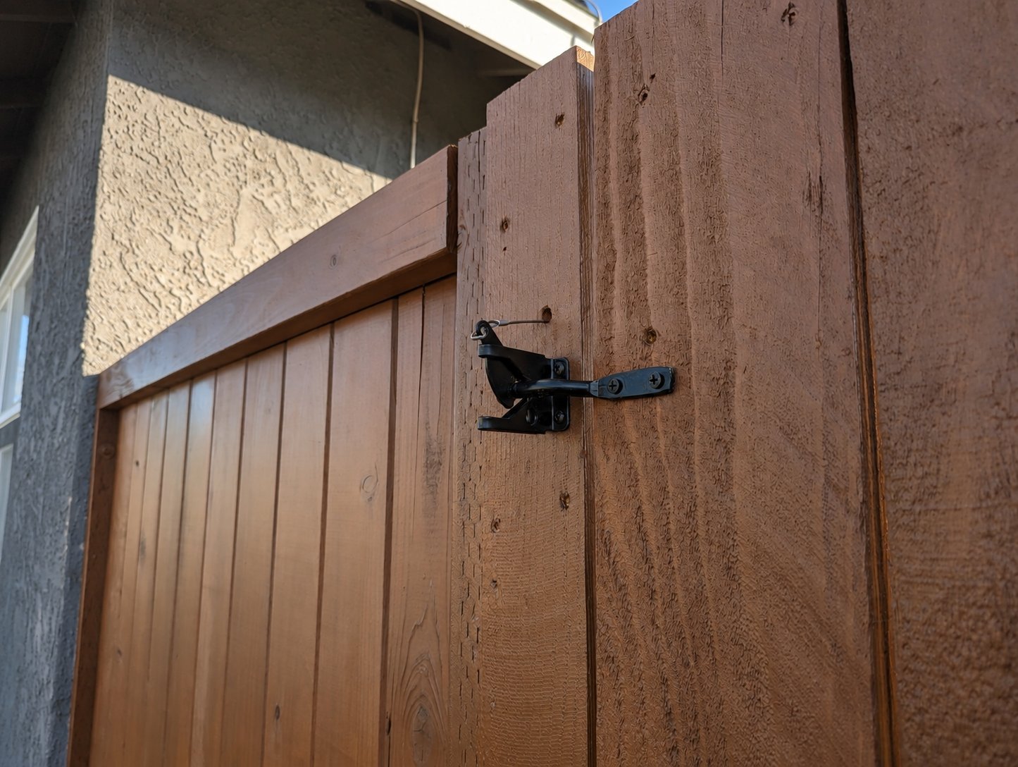 Close-up of black wrought-style gate latch hardware on stained wood side gate, modern LA backyard fence