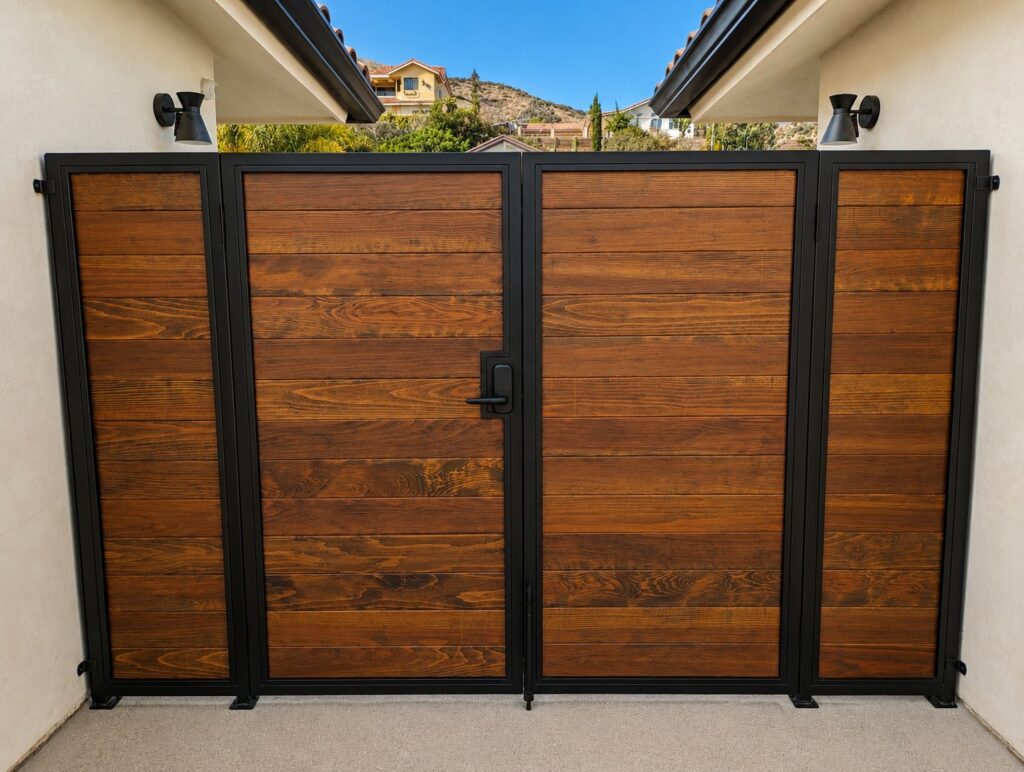 Main double driveway gate with flanking fixed panels — black steel frame, dark wood infill, LA hillside