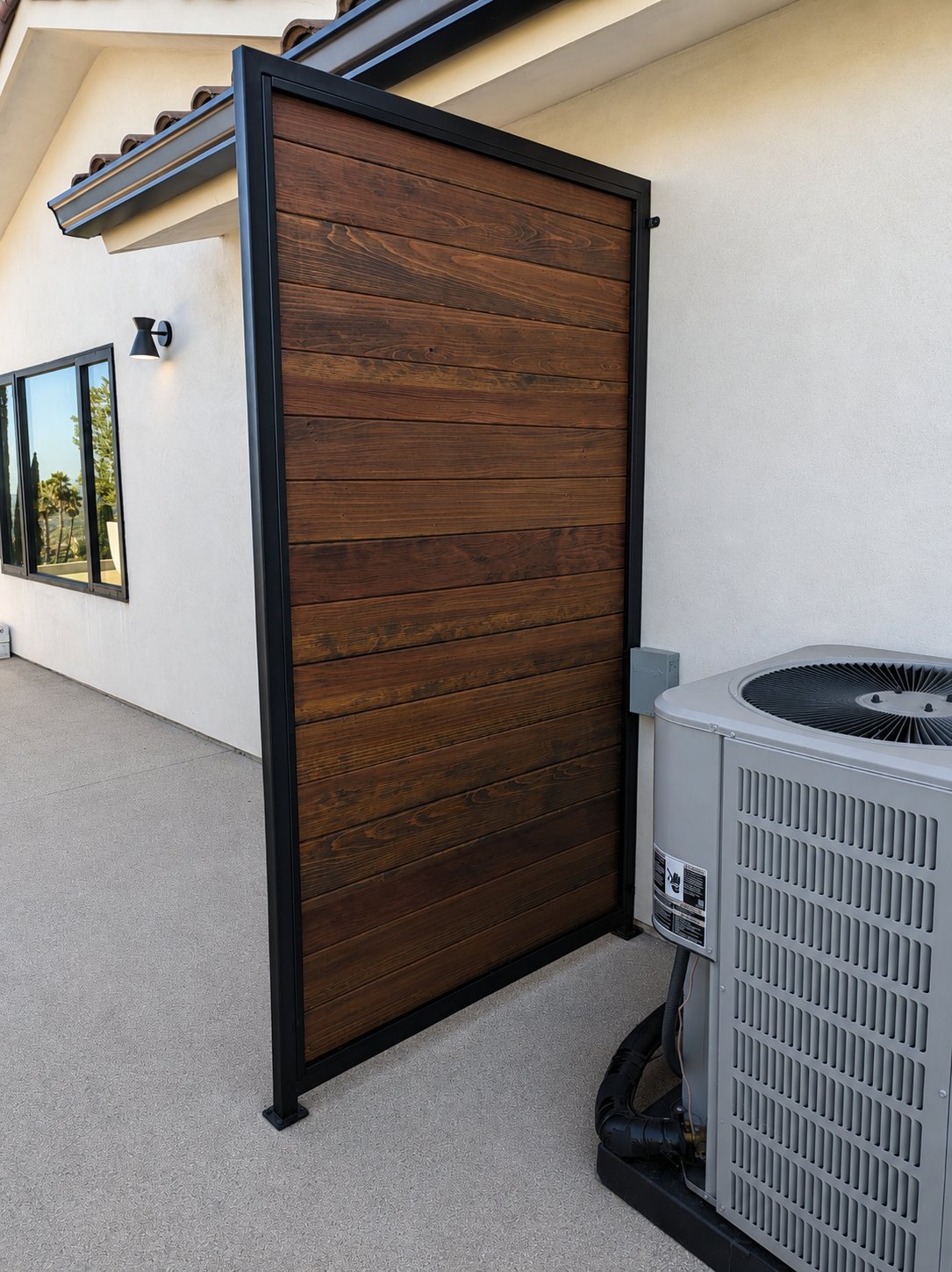 Tall opaque steel-frame wood privacy panel hiding HVAC condenser, matching gate system, LA home
