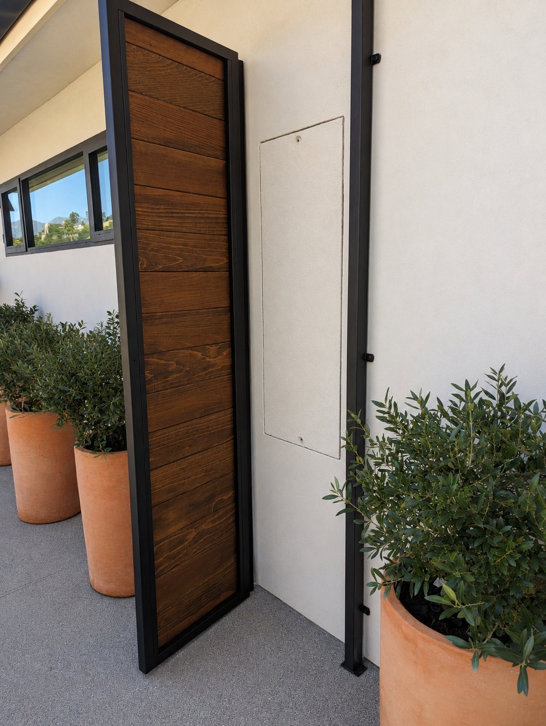 Side angle of steel-frame wood privacy panel with terracotta planters and stucco wall, LA hillside home