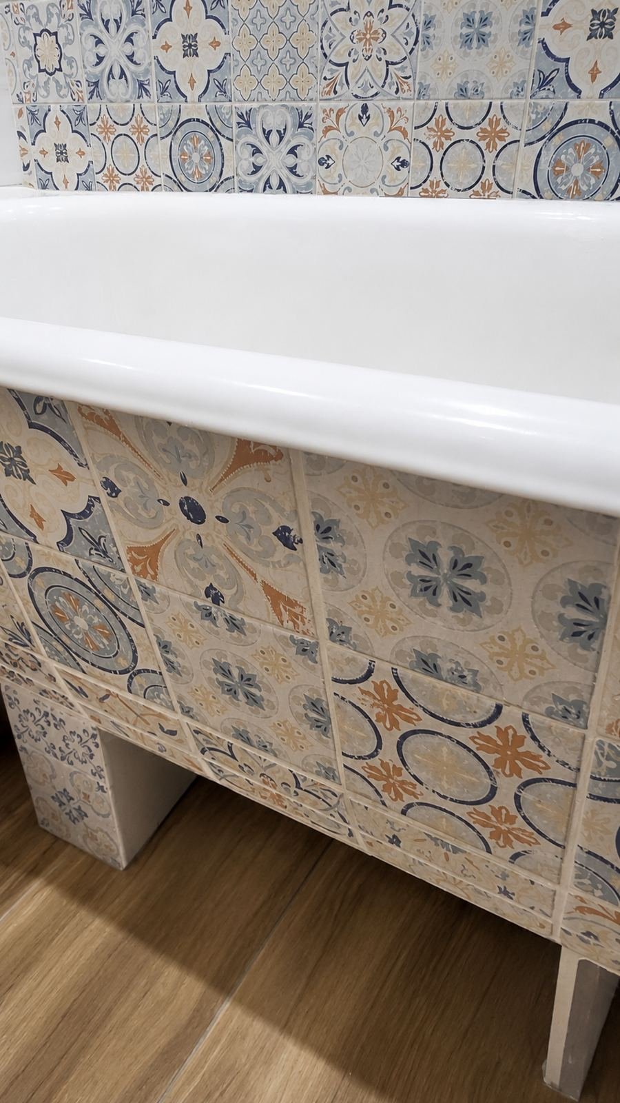 Patterned encaustic tile continued down the tub apron above wood-look ceramic plank floor — ProHands Los Angeles bathroom