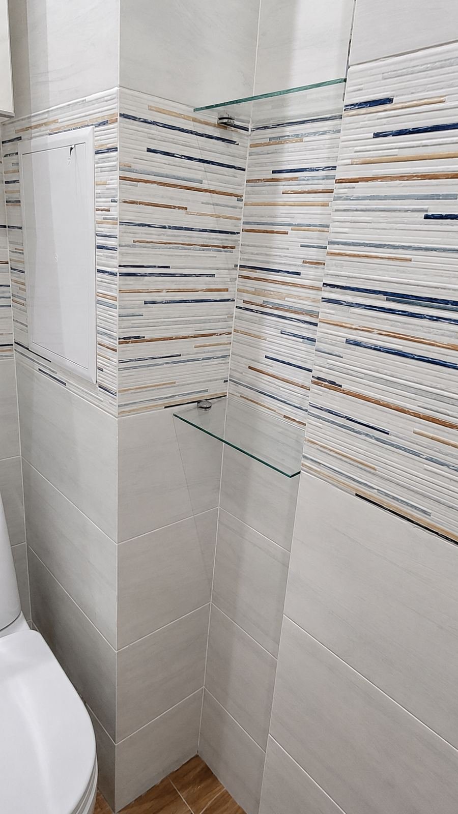Small WC bathroom remodel with horizontal glass-mosaic accent stripes and marble-look tile — ProHands Los Angeles