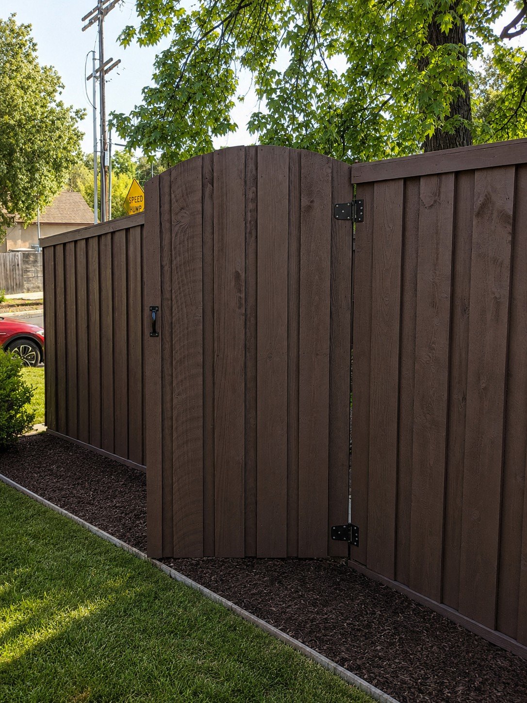 Custom arched pedestrian gate in espresso-stained board-and-batten fence — heavy black hinges and cane bolt, pull handle — ProHands Los Angeles