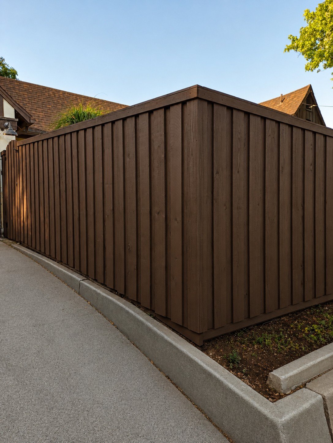 Espresso board-and-batten fence turning the driveway corner beside a Tudor Revival home — dark stain, cap rail, narrow batten reveal — ProHands Los Angeles
