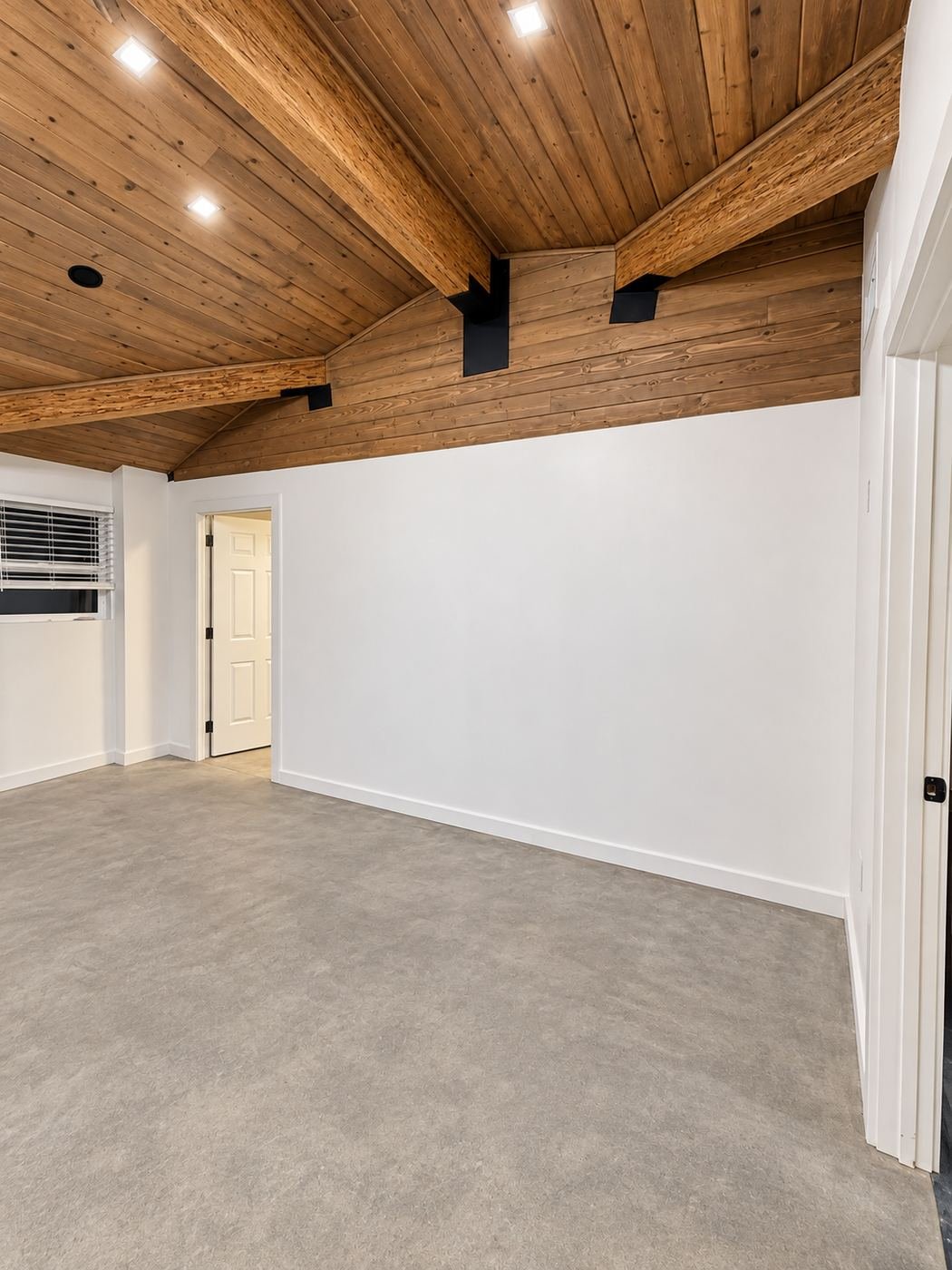 Vaulted knotty-pine shiplap ceiling with exposed engineered-wood beams on black steel brackets at a premium kitchen showroom — ProHands LA