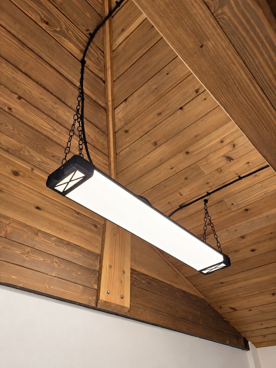 Industrial pendant light bar hung on black chains from a knotty-pine vaulted ceiling, mounted against an engineered-wood beam — premium kitchen showroom in Los Angeles — ProHands