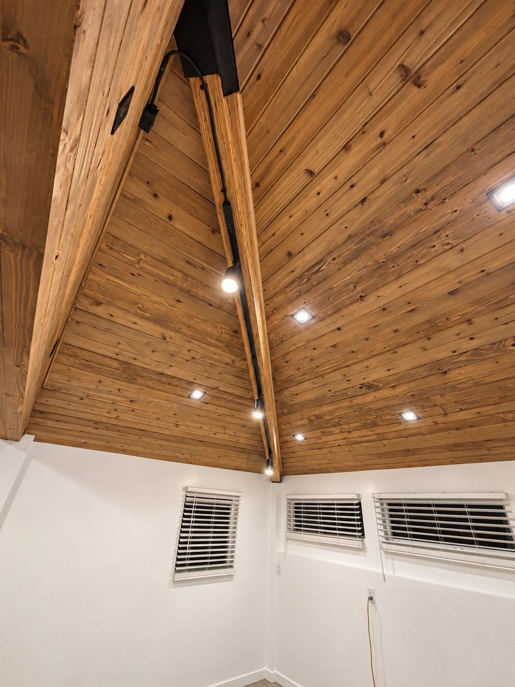 Looking up at the new vaulted knotty-pine ceiling with recessed can lights and track head, white walls below with mini-blinds — premium kitchen showroom in Los Angeles — ProHands
