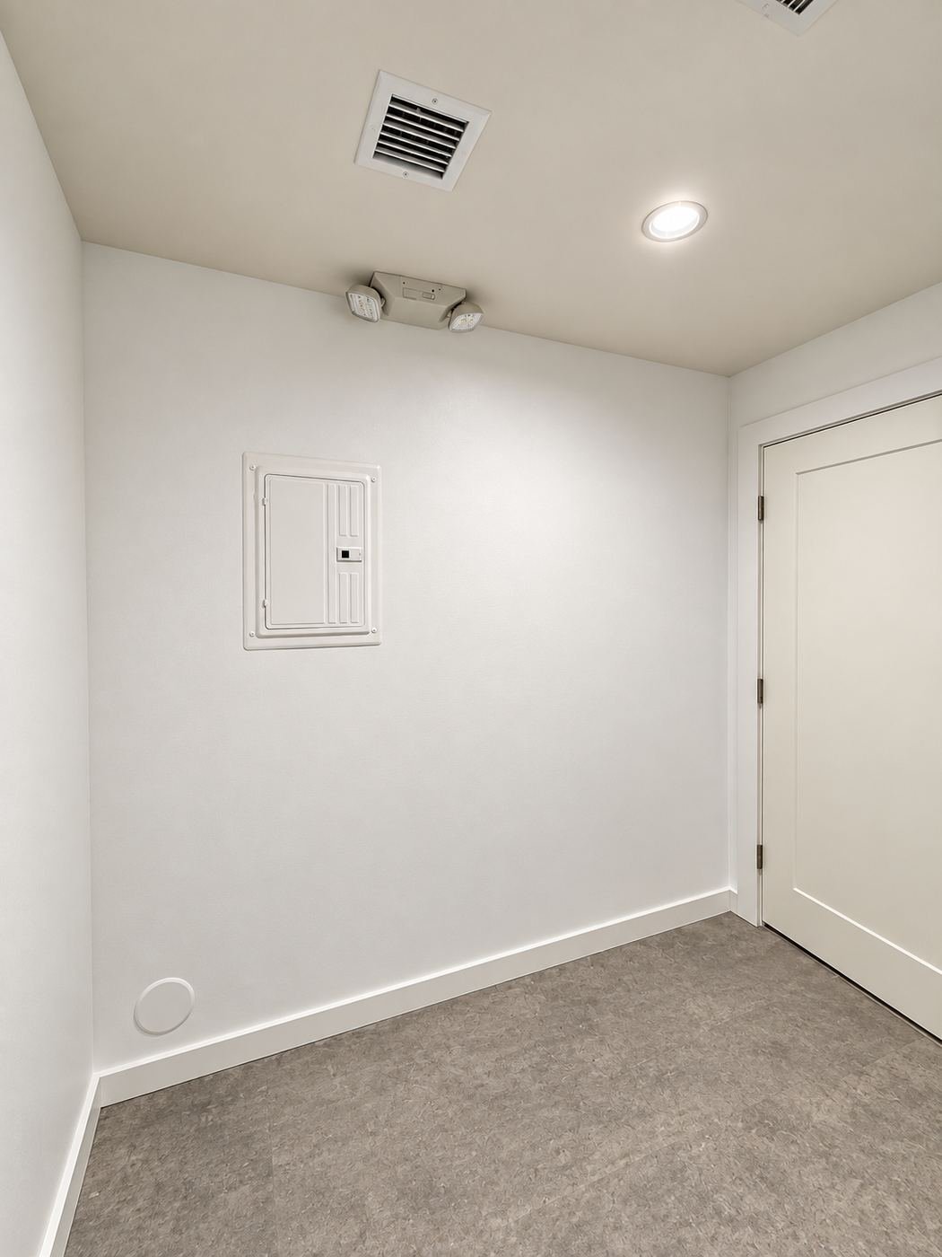 Finished electrical service room inside the showroom — flush service panel, hard-wired emergency egress light head, recessed can and HVAC vent in a clean white interior — ProHands Los Angeles