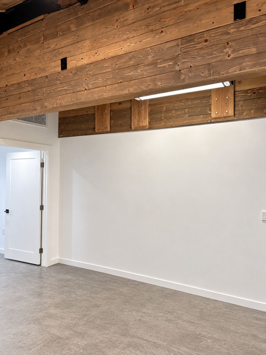 Transition from the new knotty-pine wood-clad ceiling and wall to painted white drywall, with an industrial LED bar light tucked under the wood section — ProHands Los Angeles commercial buildout