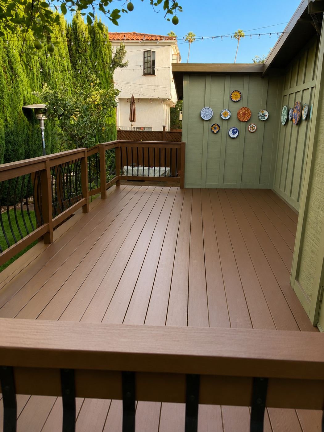 Overview of a restored wood deck with repainted warm brown finish, decorative bowed black balusters, Mexican ceramic plates on green stucco wall — ProHands Los Angeles
