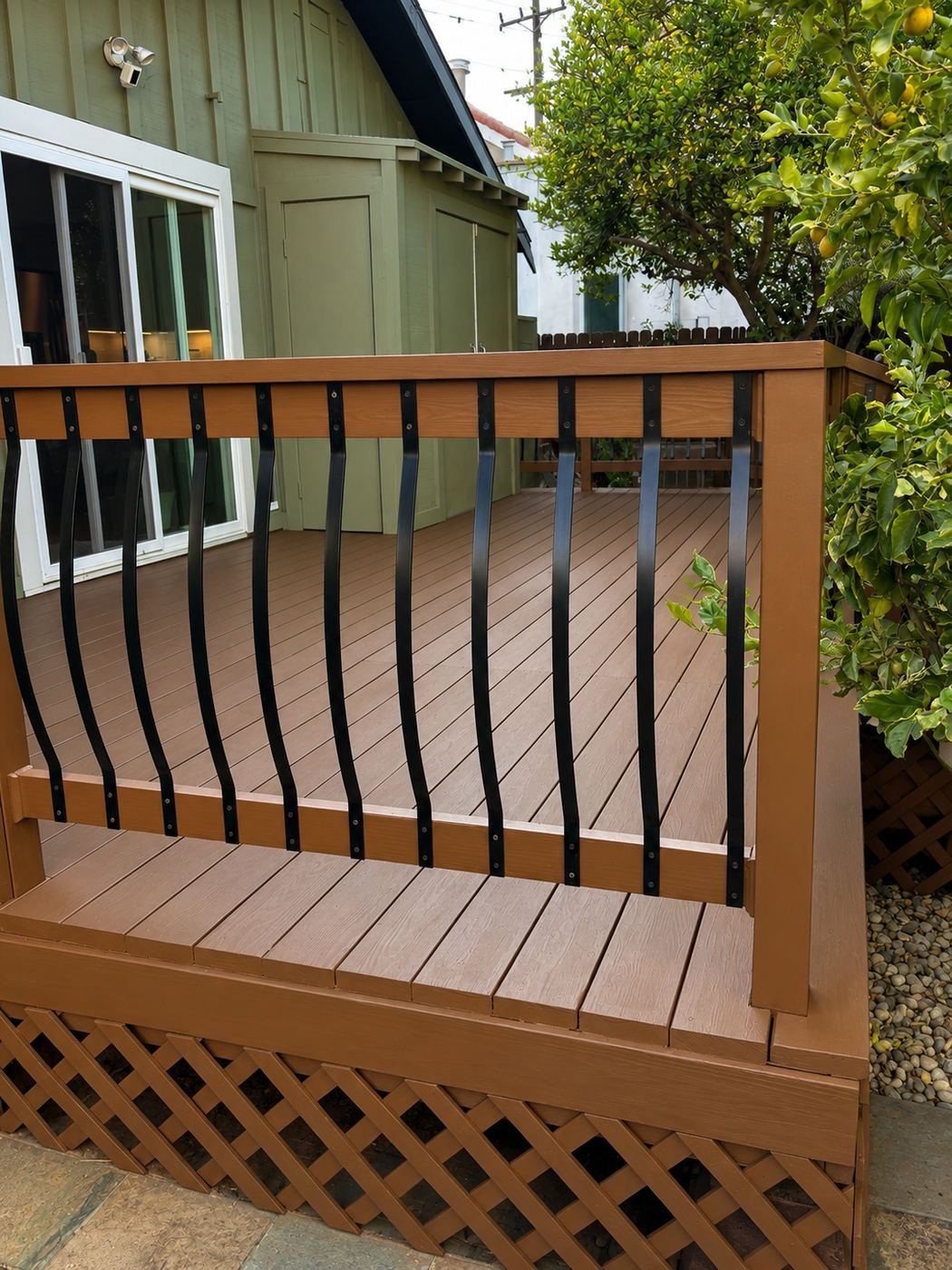 Side view of a restored wood deck with lower landing, bowed black metal balusters, lemon tree, lattice skirt and gravel apron — ProHands Los Angeles
