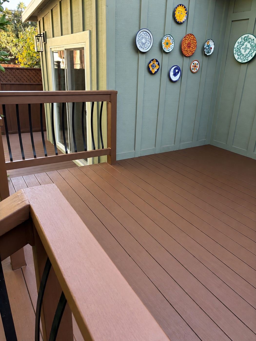 Restored wood deck floor with repainted top-rail cap, matte-black bowed balusters, Mexican plates on sage-green stucco wall — ProHands Los Angeles