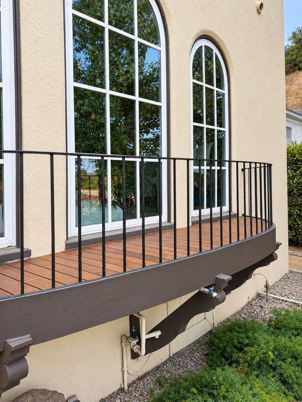 Angled side view of a curved balcony deck at a Mediterranean home — new wood boards in dark stain, iron railing, dark brown painted lower fascia and skirt panels — ProHands Los Angeles