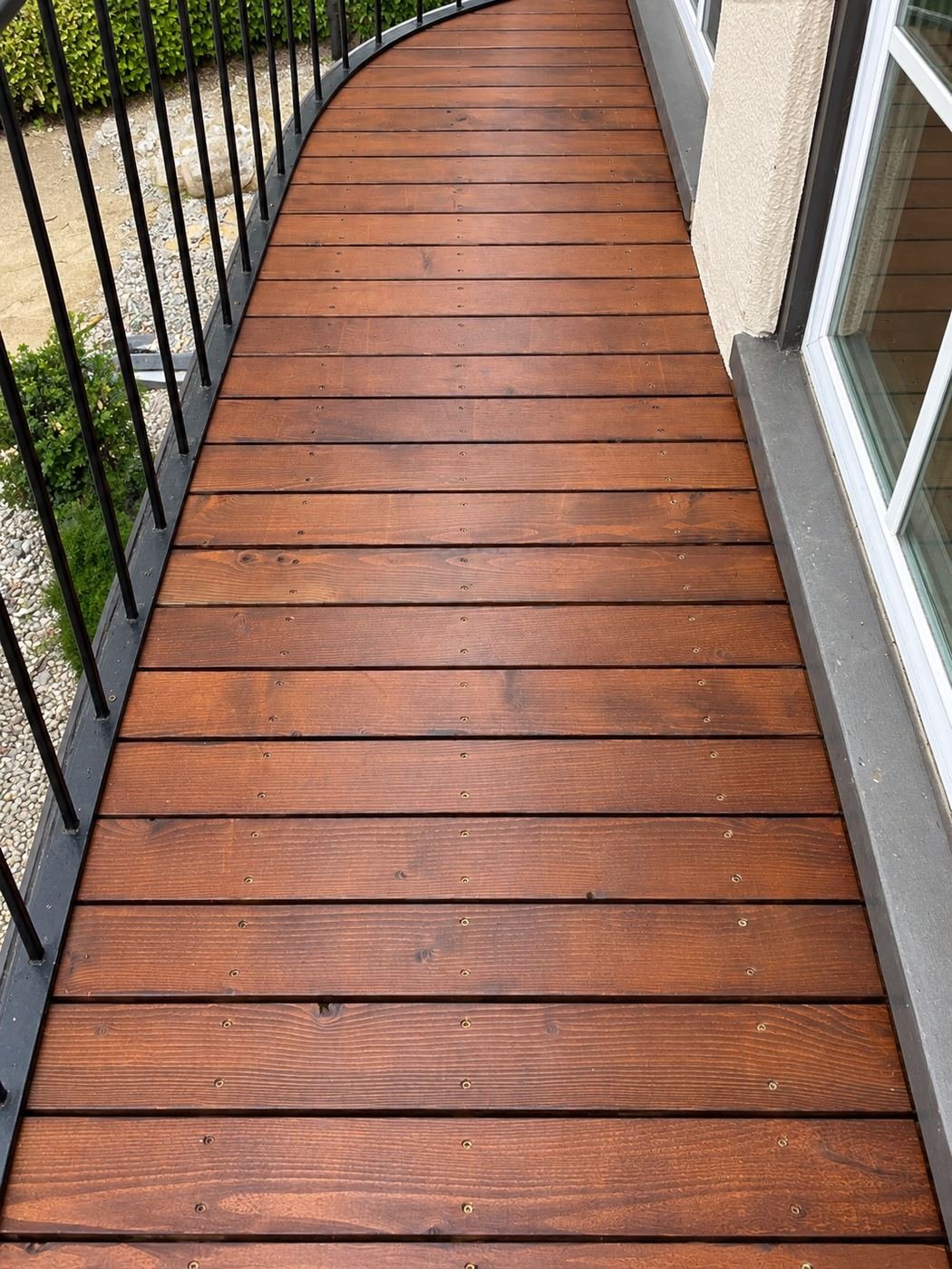Close detail of the new wood deck boards in espresso stain on a curved balcony — iron railing posts, visible countersunk screws, Los Angeles — ProHands