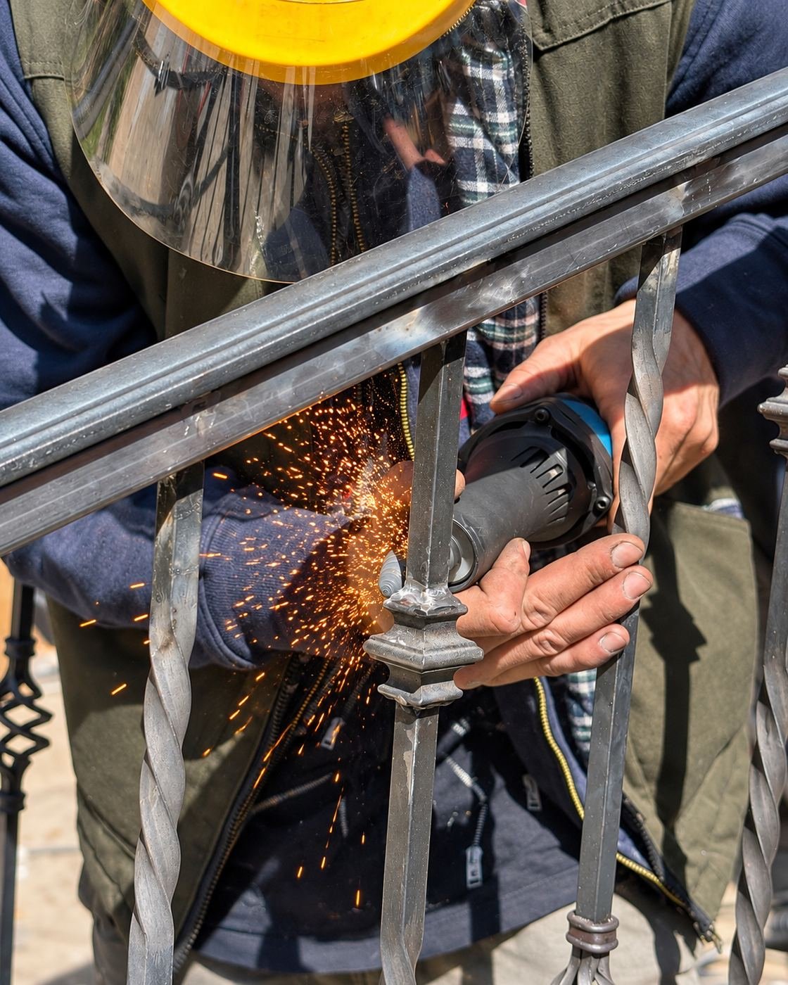ProHands welder in our shop grinding a weld on a raw wrought-iron handrail frame with sparks flying — in-house fabrication of the handrails for this project