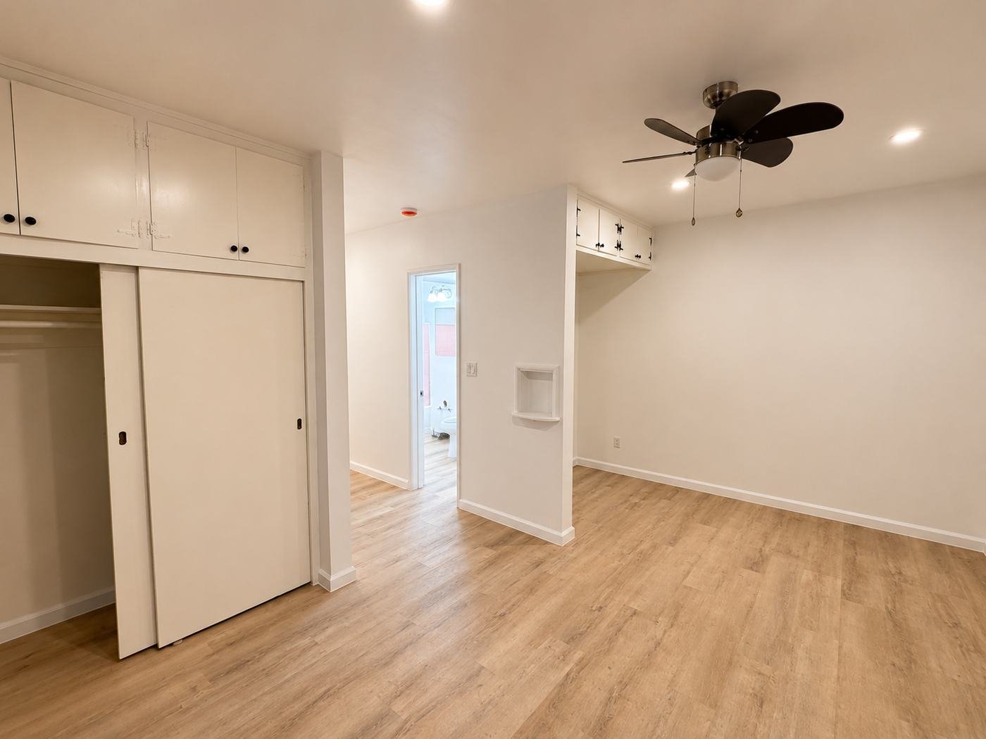 Finished apartment living area after full remodel in Los Angeles — new LVP floor, repainted period built-in cabinets with black hardware, white walls, ceiling fan, sliding closet doors — ProHands