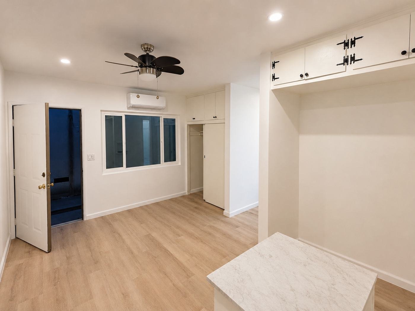 Finished living room of a Los Angeles apartment remodel with new LVP floor, white walls, repainted built-in cabinets, mini-split AC, ceiling fan and marble-top island — ProHands