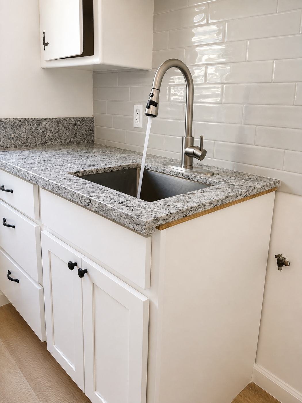New kitchen counter in a Los Angeles apartment remodel — quartz-marble countertop, white Shaker cabinets with black pulls, stainless pull-down faucet, white subway backsplash — ProHands