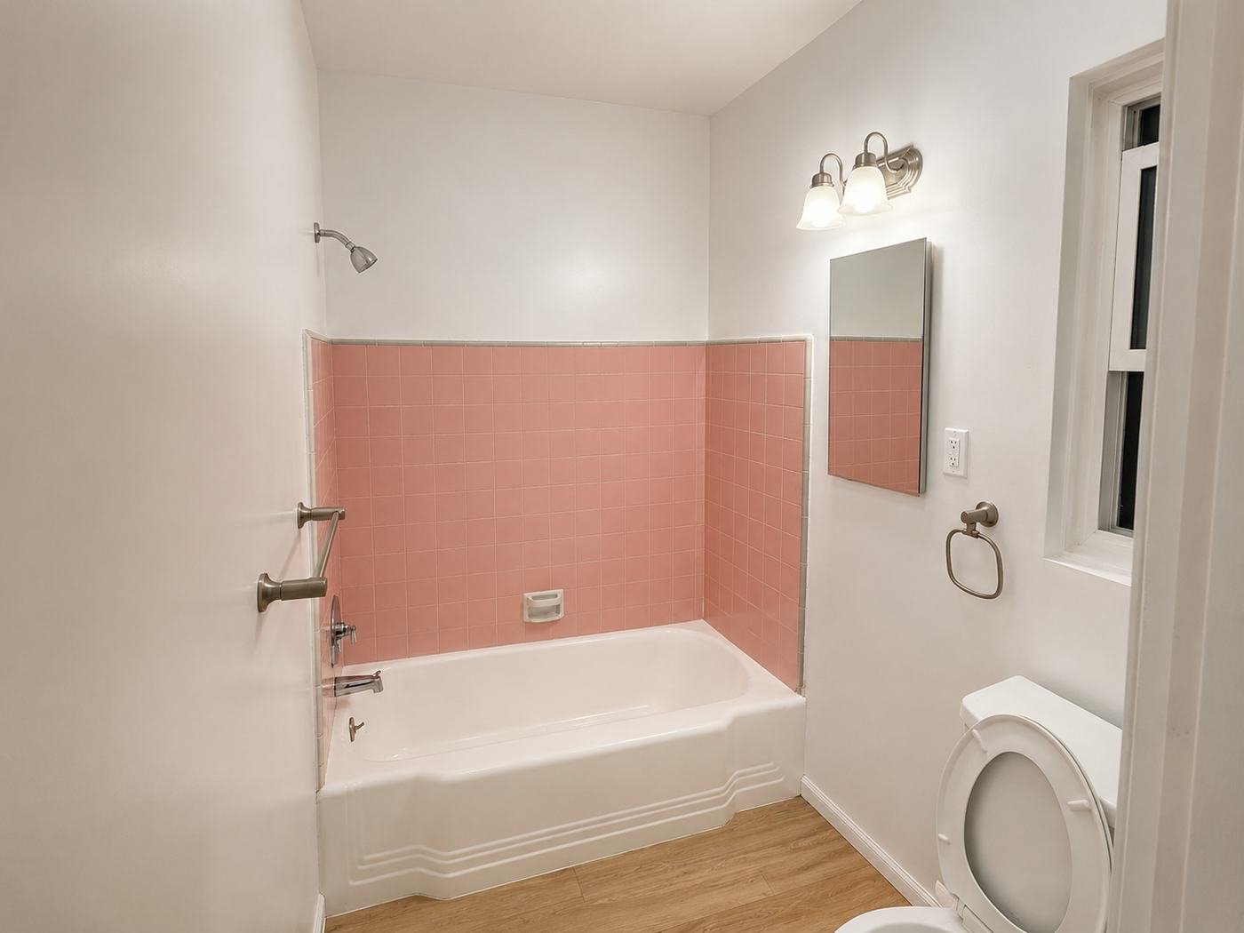 Finished bathroom after full remodel — vintage pink wall tile preserved, bathtub refinished in white, new water-resistant wood-look plank floor, new fixtures — ProHands Los Angeles