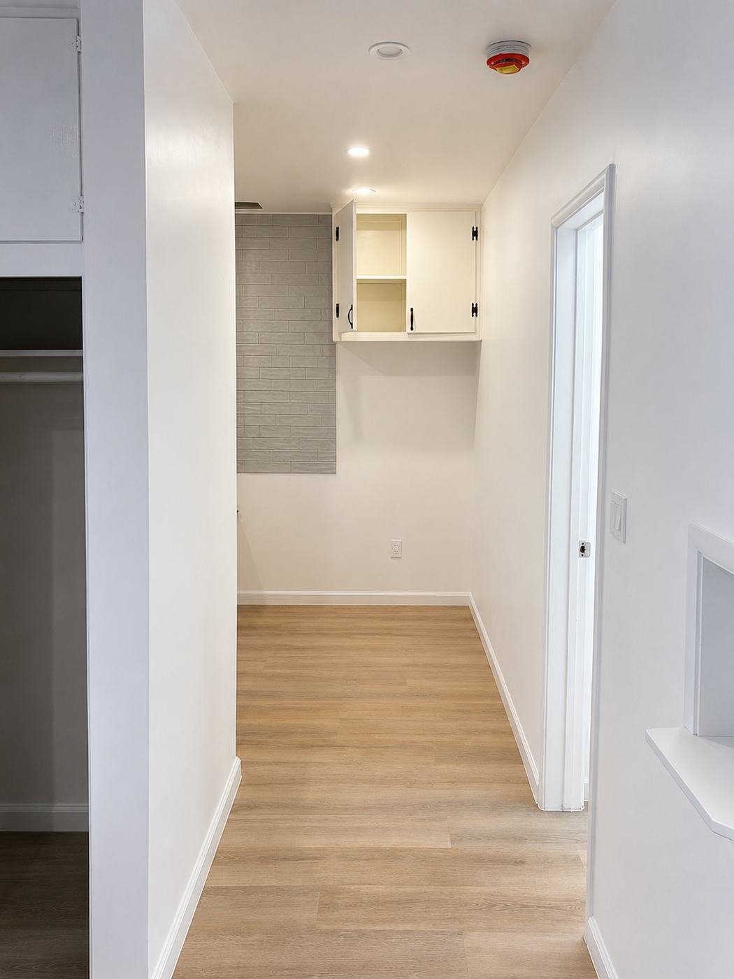 Hallway and kitchenette after full apartment remodel — grey subway tile accent wall, repainted built-in cabinets, new LVP floor and fresh paint — ProHands Los Angeles