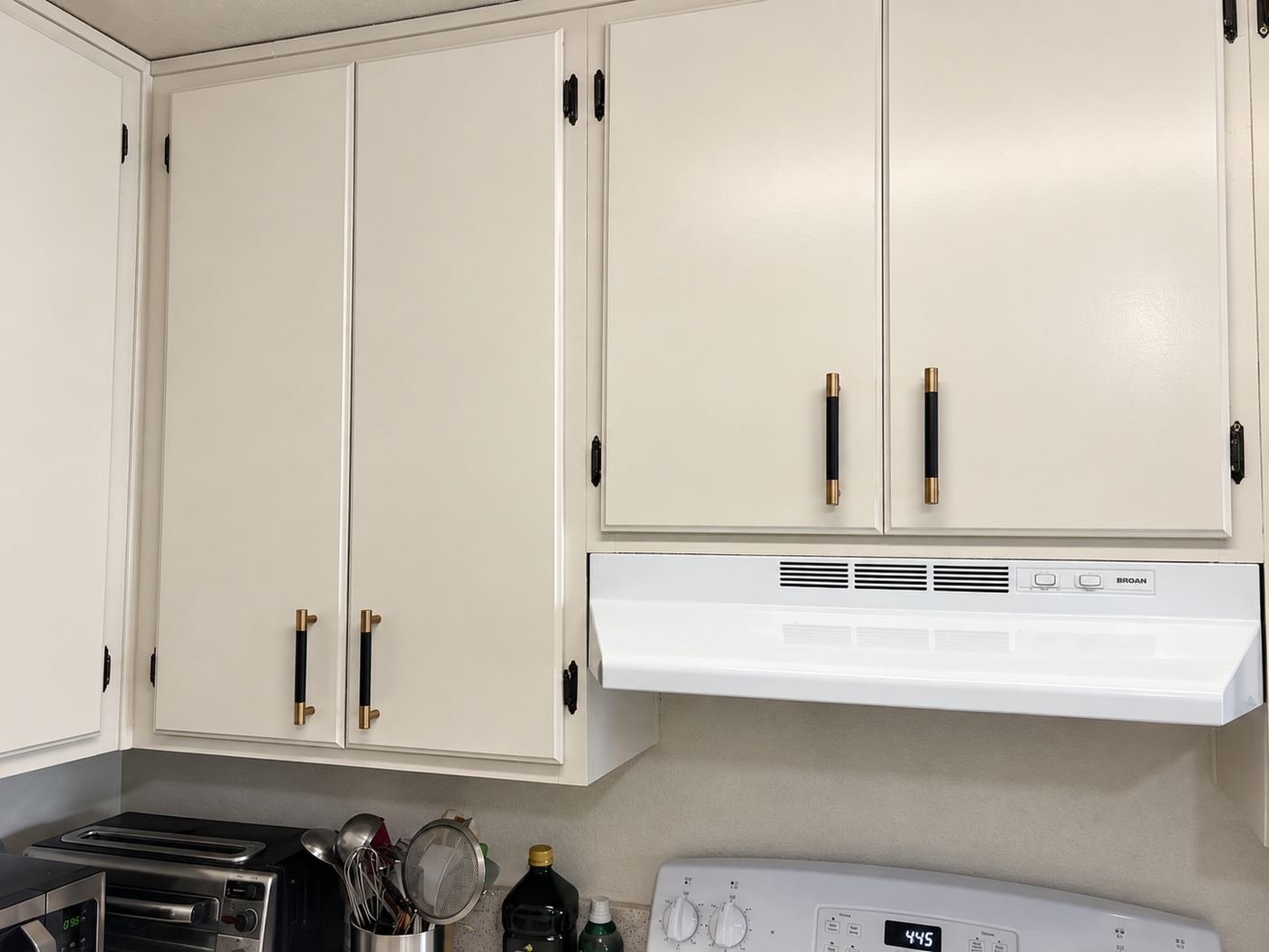Detail of warm-white refinished kitchen cabinets with new black-and-brass bar pulls, original black hinges, and a new white BROAN range hood — ProHands Glendale
