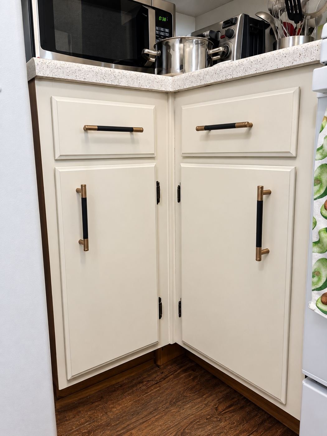 Corner lower cabinets in warm white with new black and brushed-brass bar pulls and original black hinges, speckled quartz counter above, Glendale — ProHands
