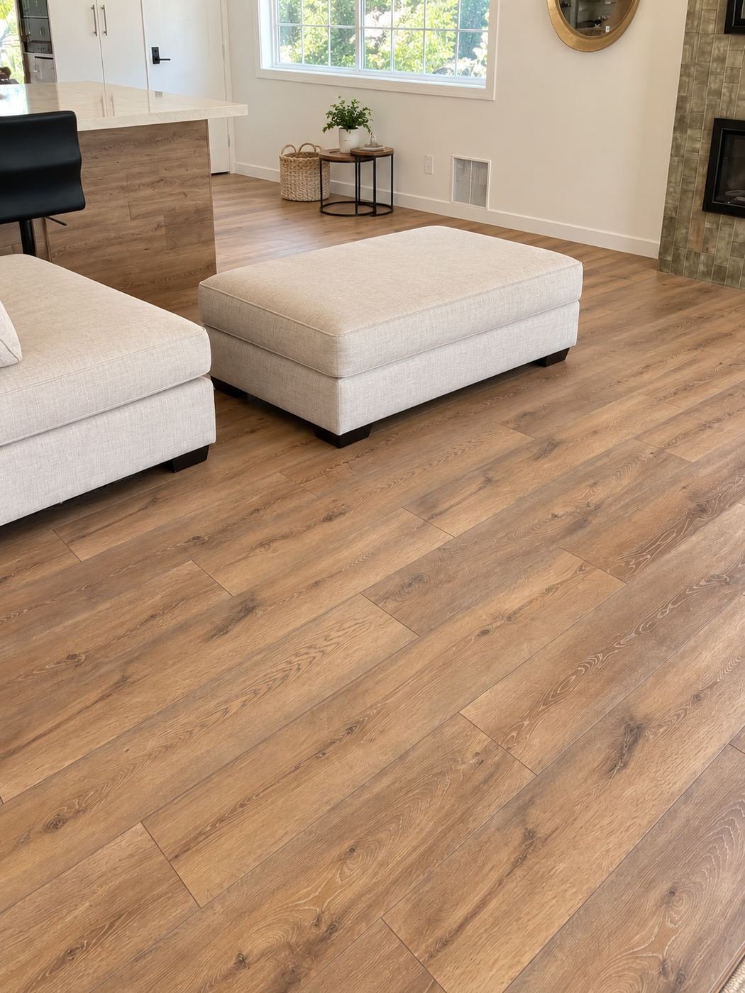 Living room with the same wide-plank warm-oak LVP floor running continuously into the kitchen area, white sectional ottoman, side table, plant and a tiled fireplace — ProHands 2,800 sq ft one-field flooring install, Los Angeles