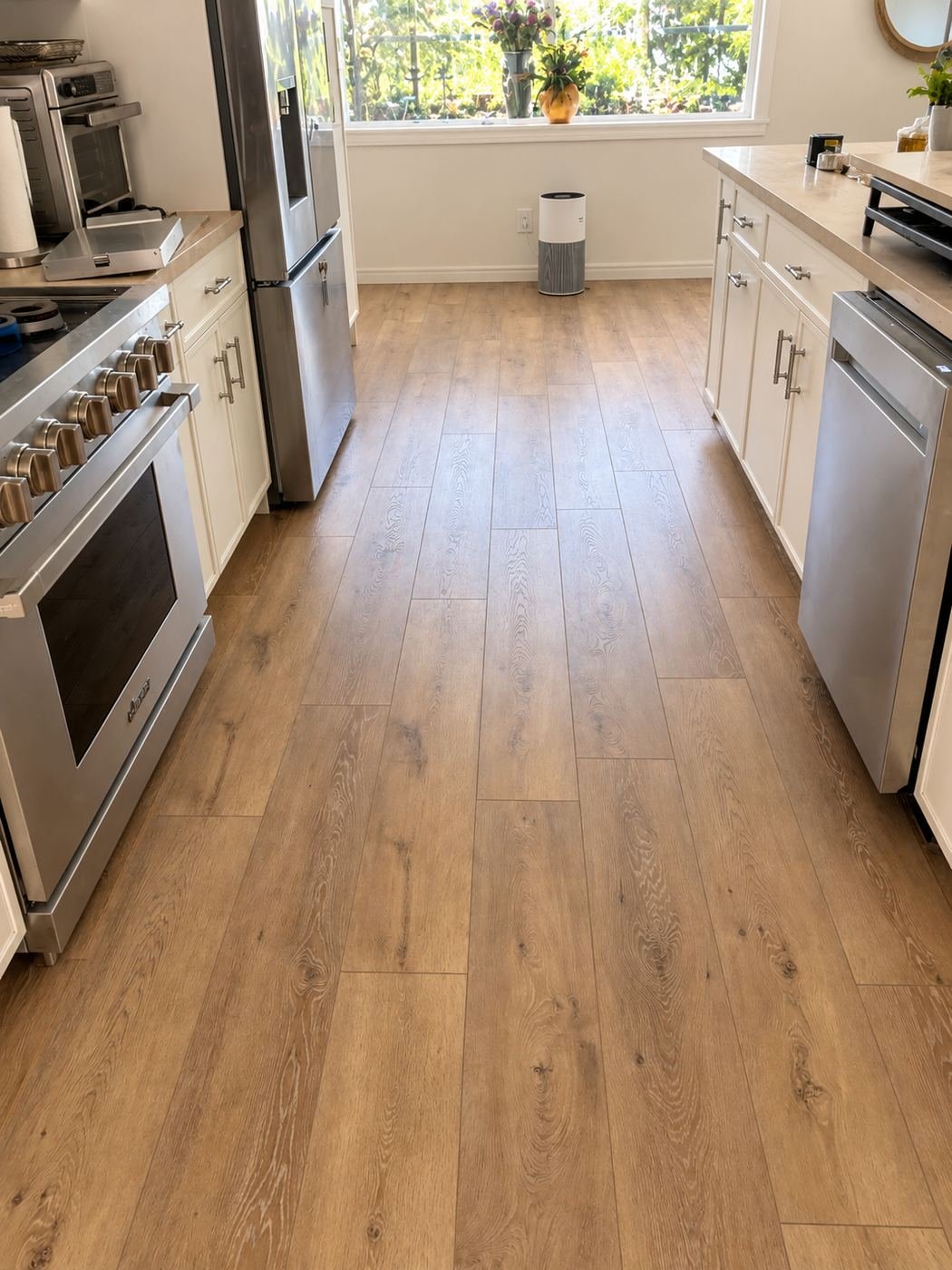 Galley kitchen with the warm-oak LVP flowing under a Dacor range, stainless fridge and dishwasher — same continuous floor as the rest of the house — ProHands 2,800 sq ft one-field install, Los Angeles