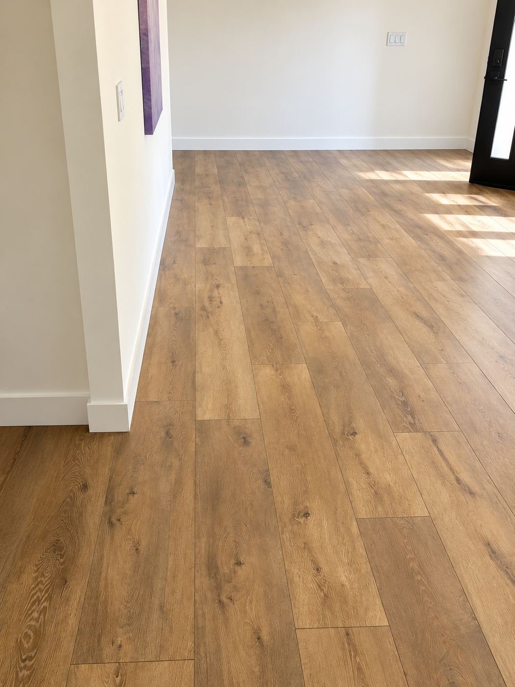 Open living area looking toward a black entry door — wide-plank warm-oak LVP floor fills the whole room without transitions — ProHands 2,800 sq ft one-field flooring install, Los Angeles