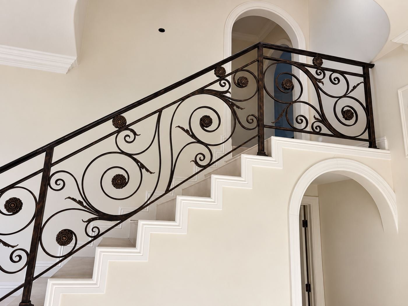Interior staircase landing with a custom-fabricated wrought-iron railing full of scroll ornaments, cream-painted walls and crown molding — Mediterranean mansion remodel, Los Angeles — ProHands
