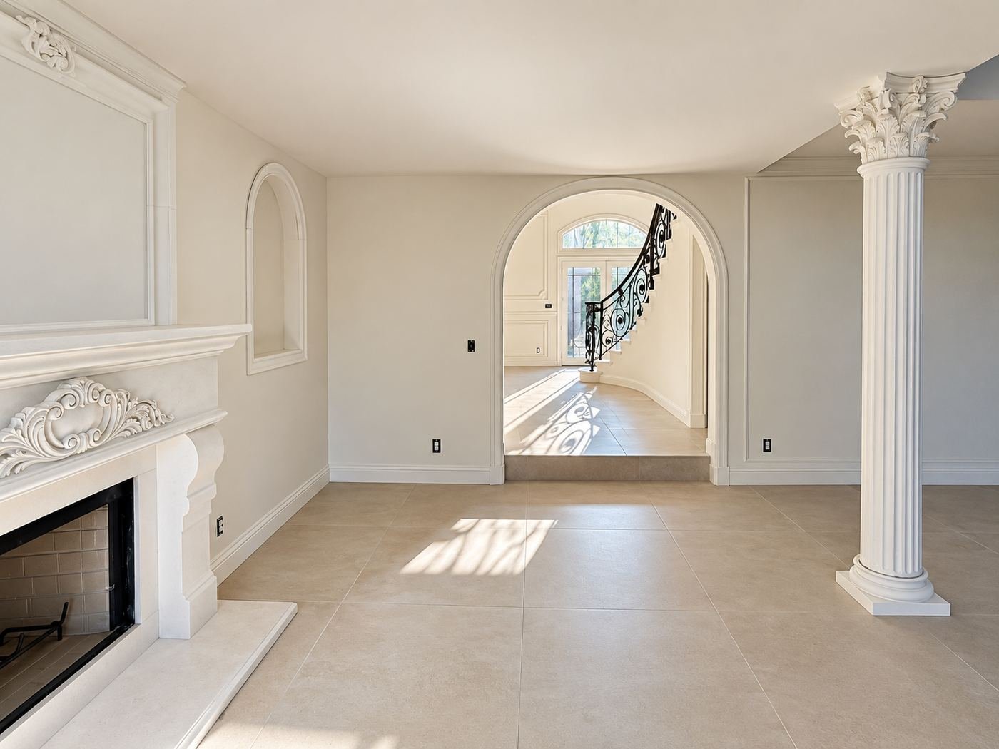 View through a formal arched opening to the main living area — Corinthian column, ornate limestone fireplace, travertine floor and a glimpse of the wrought-iron staircase railing in the distance — ProHands mansion remodel, LA