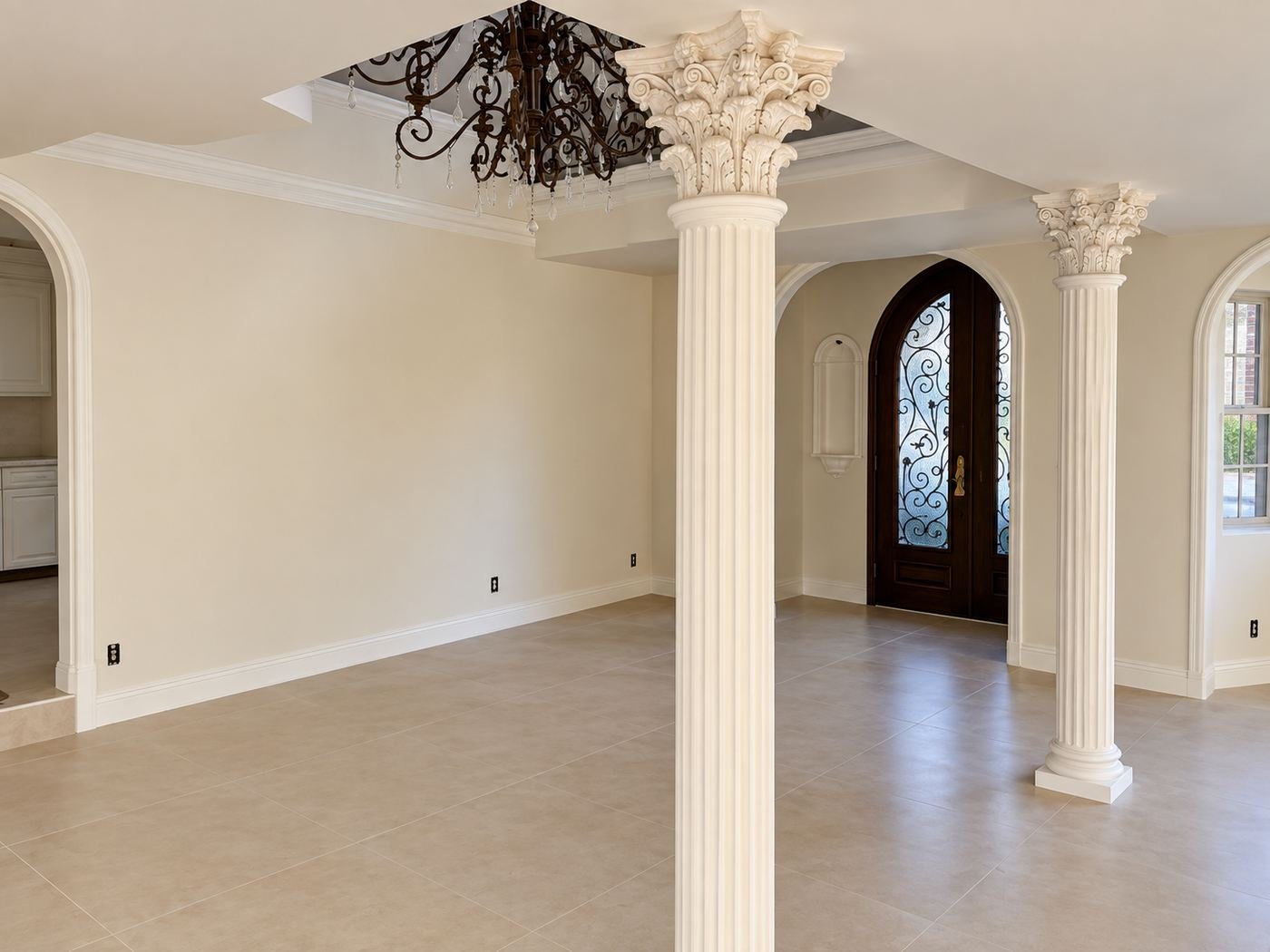 Grand formal reception with a Corinthian column and matching column visible through the arch, large wrought-iron chandelier, raised-panel wainscot and view through an arched iron door at the back — Mediterranean mansion remodel LA