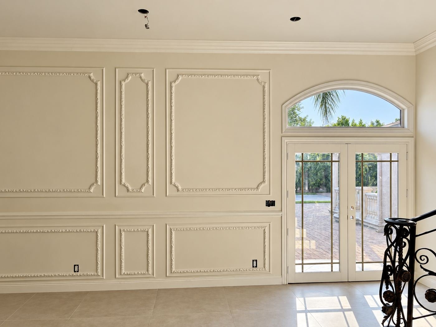 Formal room with raised-panel wainscot on every wall, large arched window with iron grille, French door to the garden — Mediterranean mansion remodel, LA