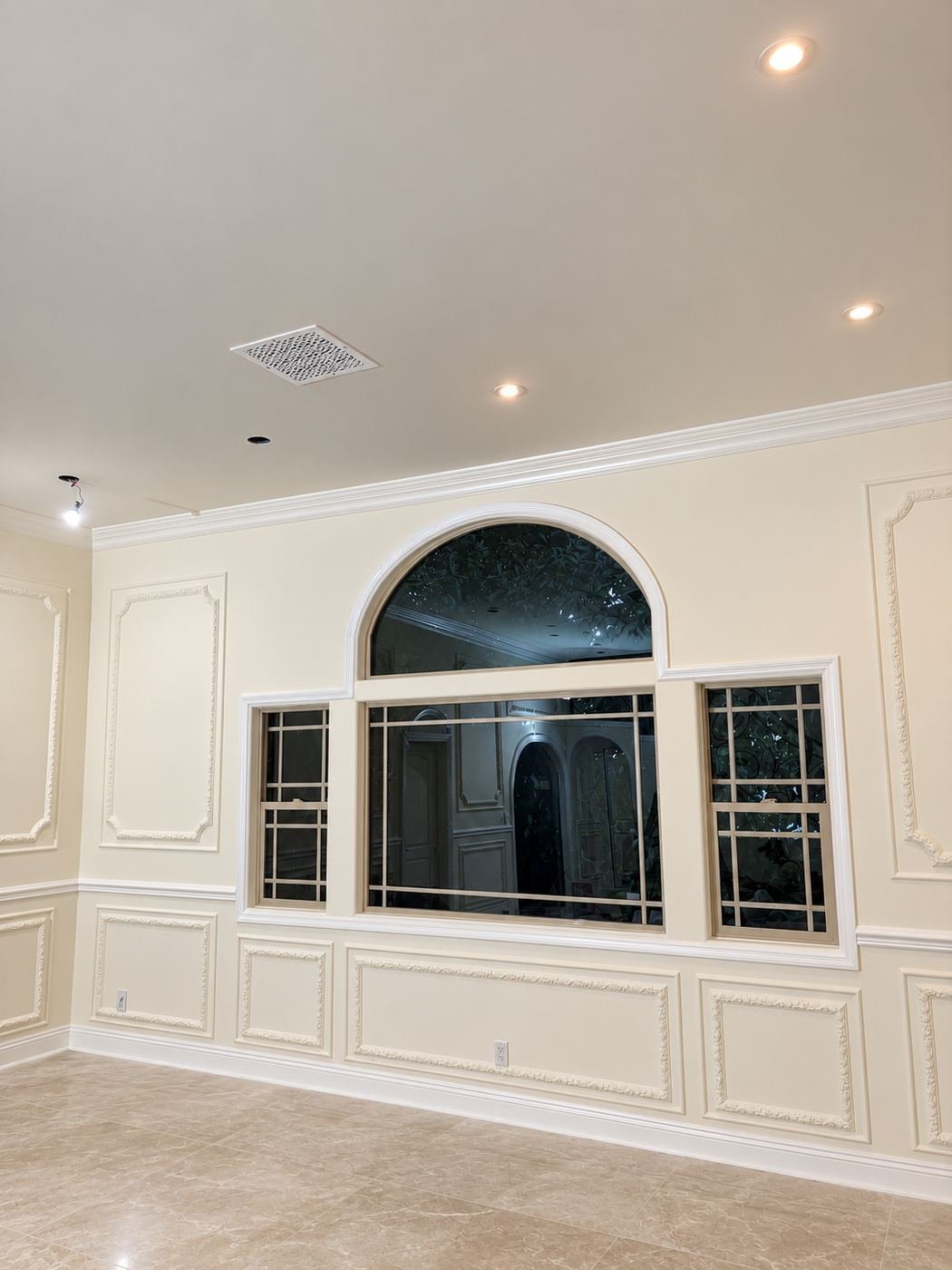 Formal room with raised-panel wainscot, white crown molding and a large arched window with view to the garden — Mediterranean mansion remodel, Los Angeles