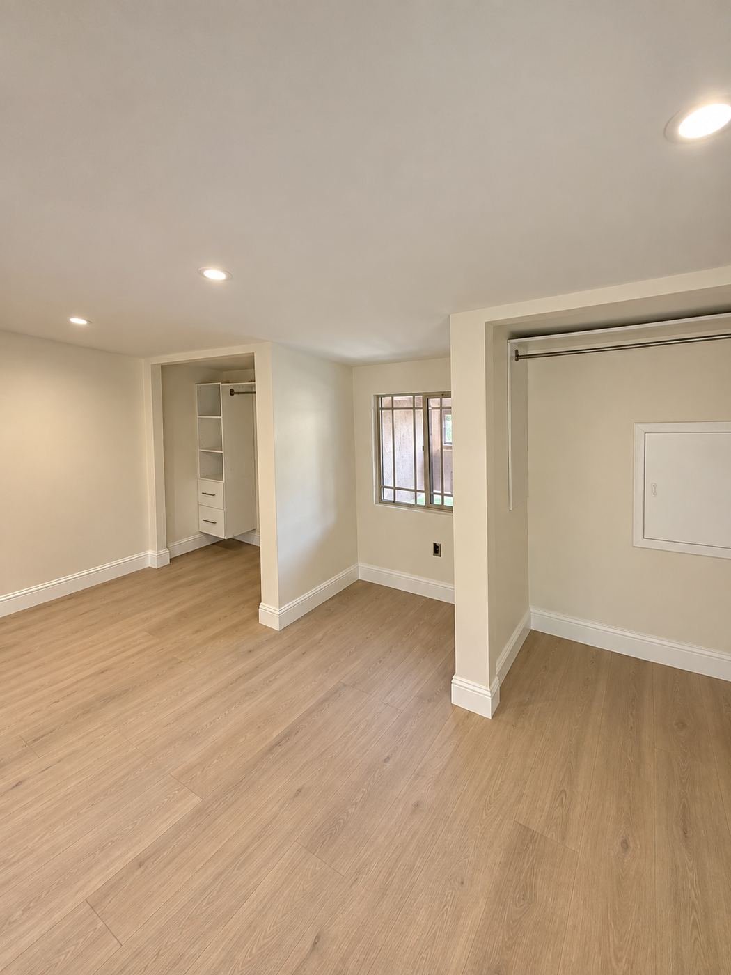Secondary bedroom with light-oak floor, warm cream paint and a closet opening — Mediterranean mansion remodel, Los Angeles
