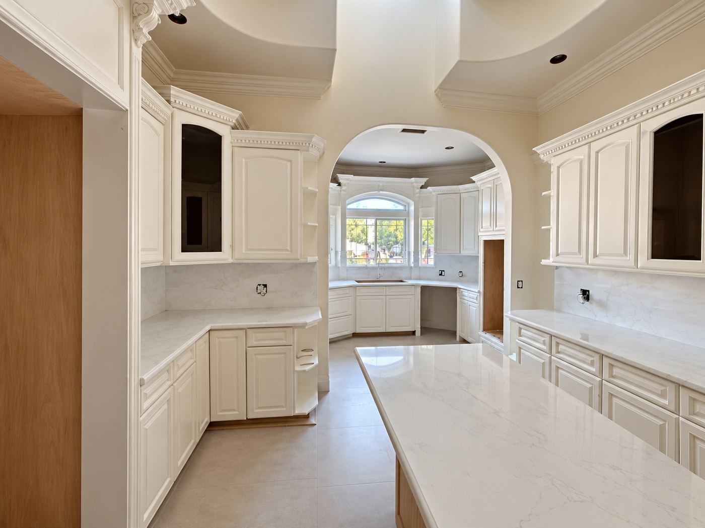 Dual-island kitchen in a Mediterranean mansion — cream cabinets, white quartz, arched doorway — ProHands LA