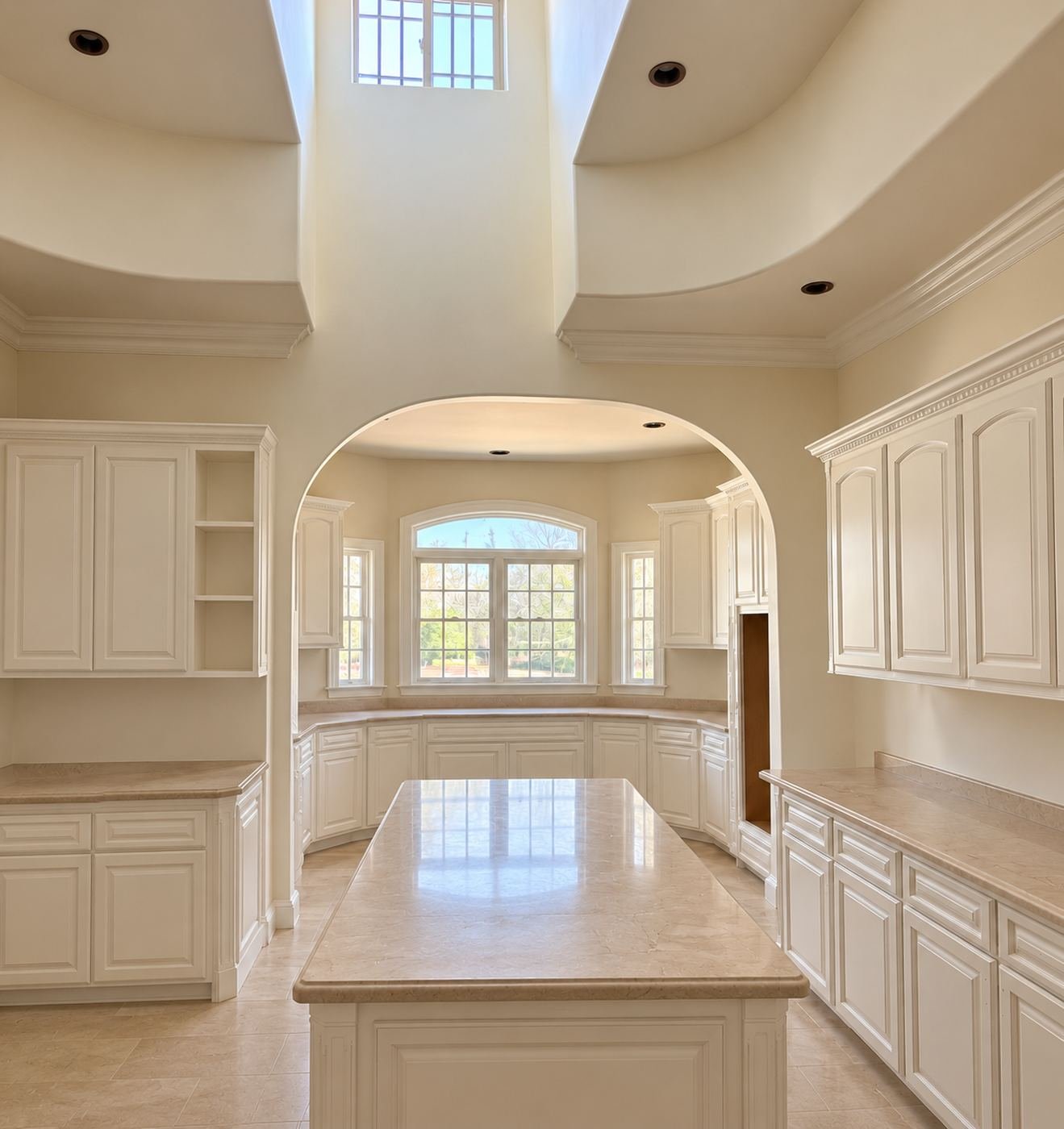 Approach to the main kitchen island of the mansion remodel — cream raised-panel cabinets, white quartz, arched doorway and crown-molded transom at the back — ProHands LA