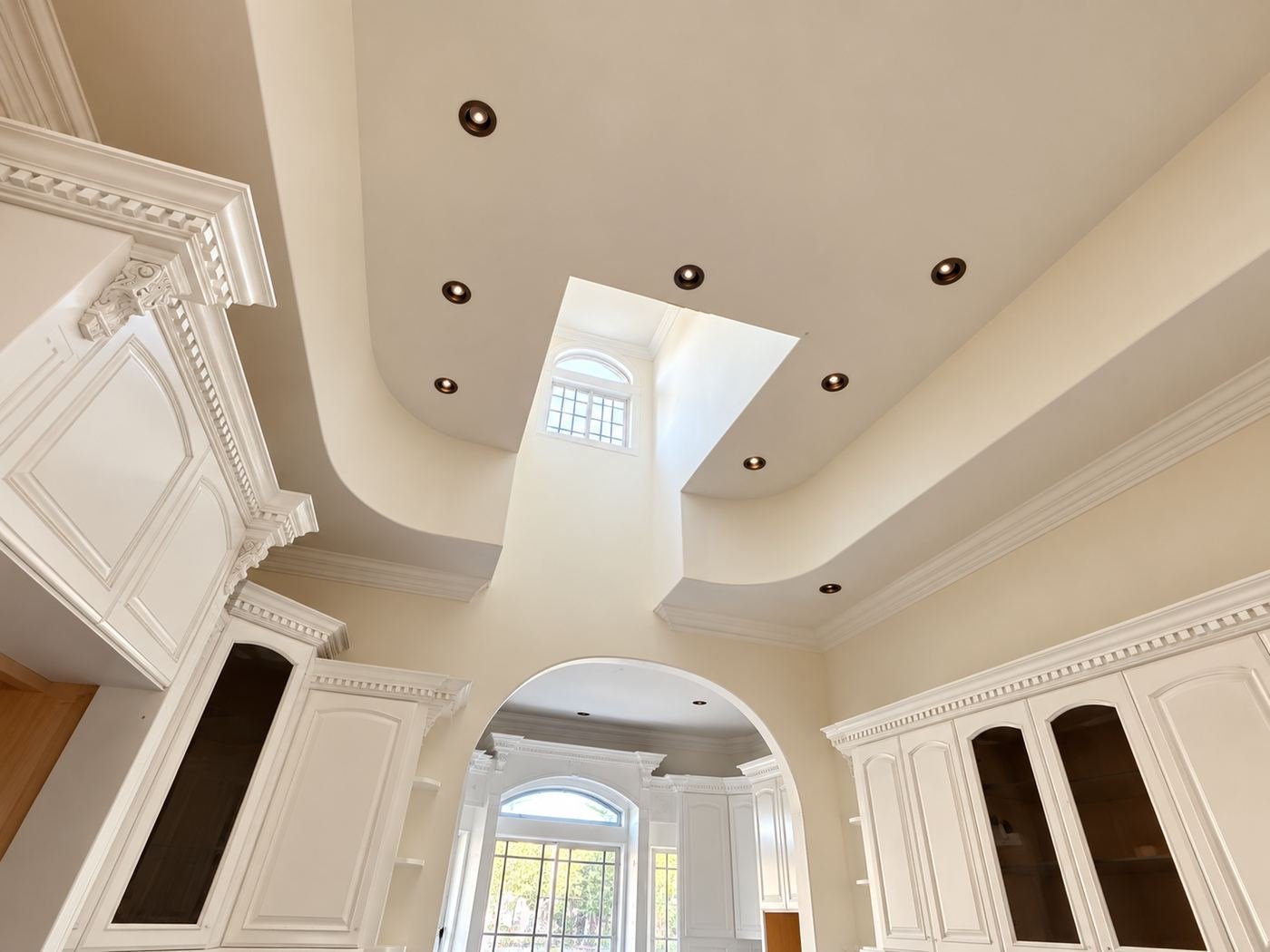Looking up at the kitchen ceiling of the mansion — ornate crown molding transition, recessed can lights and an arched opening down to the next room — Chapter 3 kitchen, LA