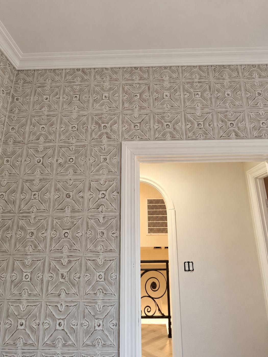 Tin-tile powder-room wall looking through a doorway toward a wrought-iron door and the formal rooms beyond — ties the bath finish to the rest of the mansion — ProHands LA