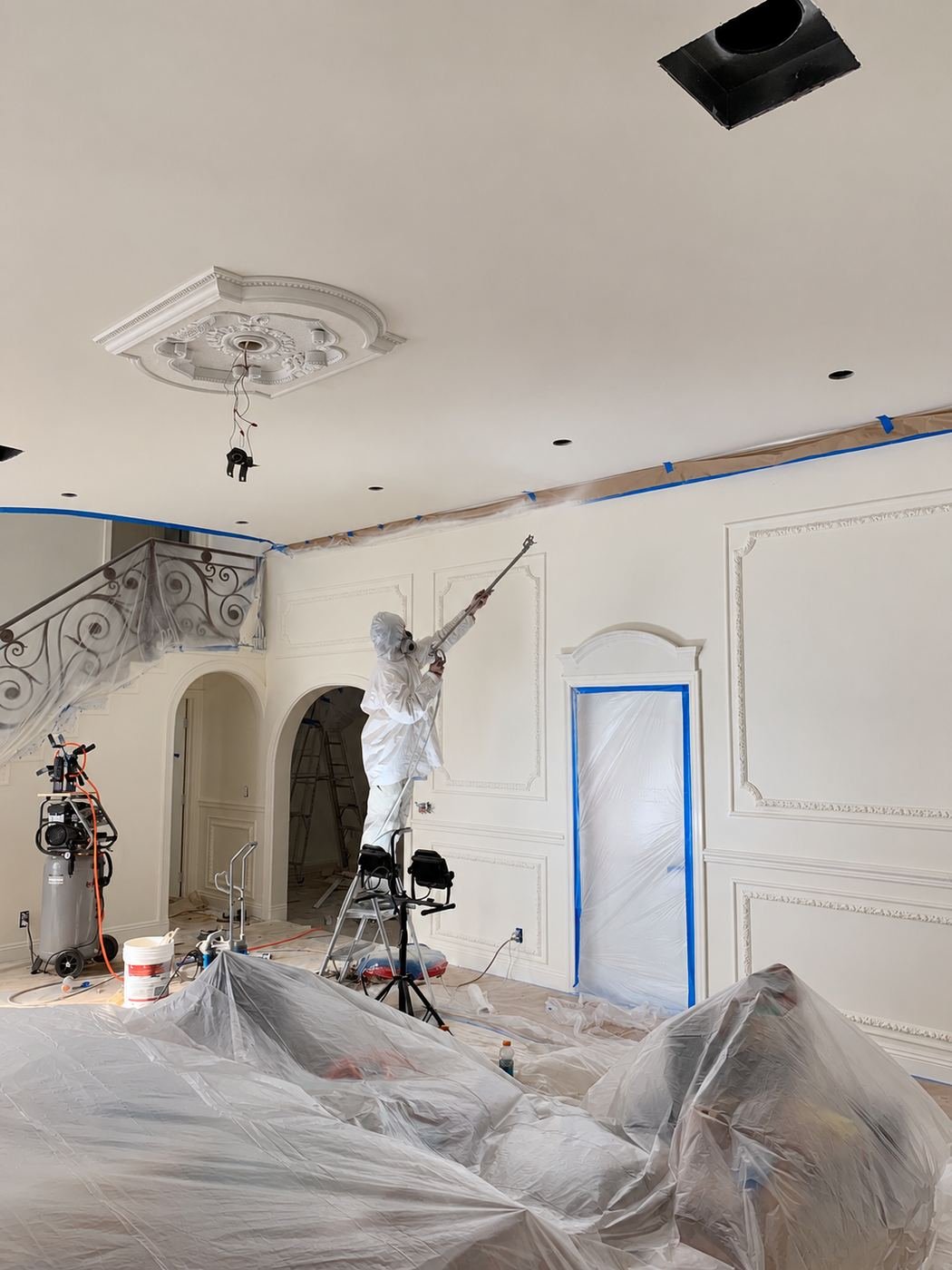Close-up of a worker in a respirator finishing the carved ornament of an ornate limestone fireplace mantel with a small spray gun — plastic sheeting protecting the firebox opening — Mediterranean mansion remodel, Los Angeles