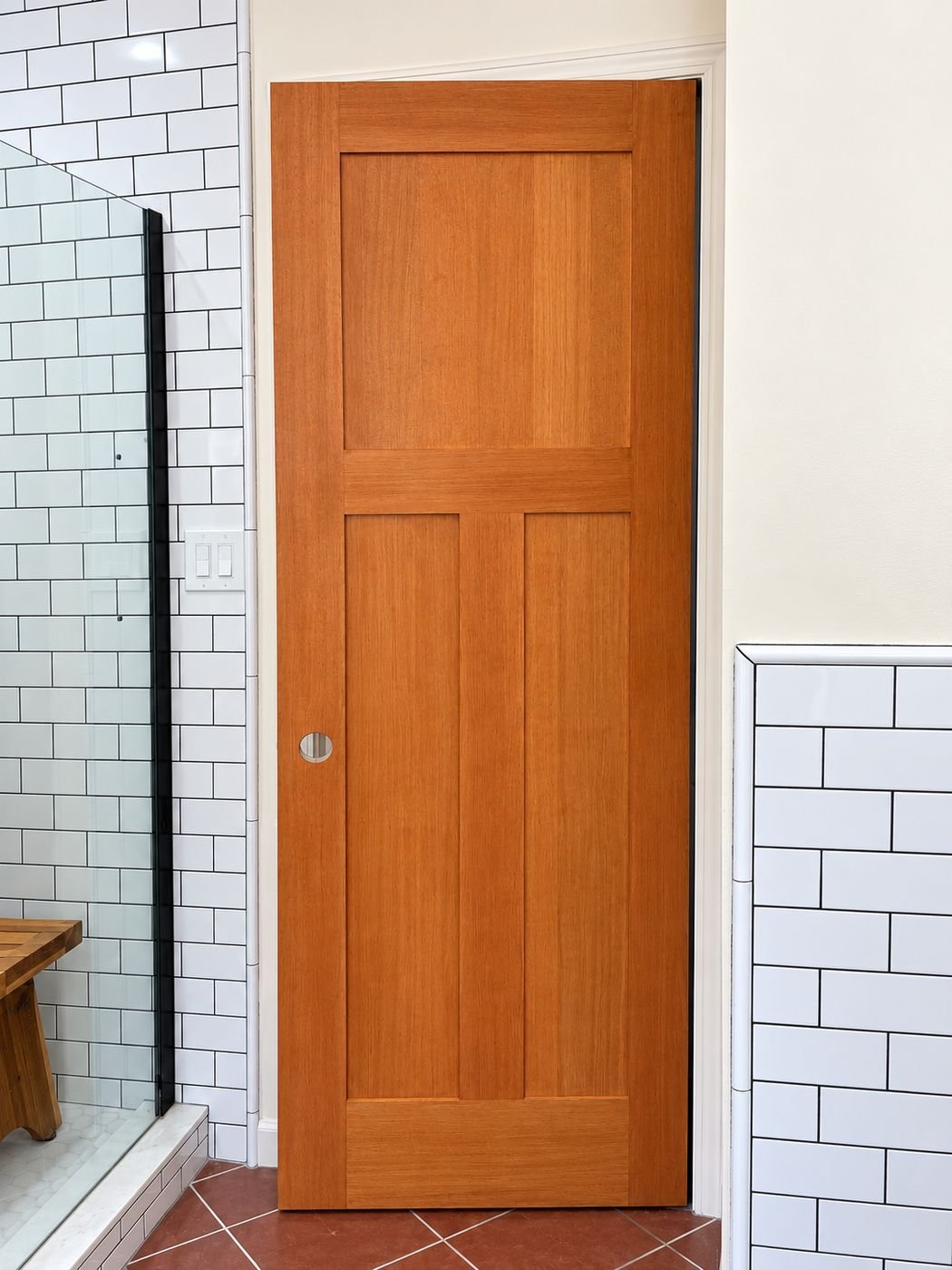 Solid wood four-panel Craftsman interior bathroom door closed, honey stain finish, between white subway tile walls — ProHands Los Angeles