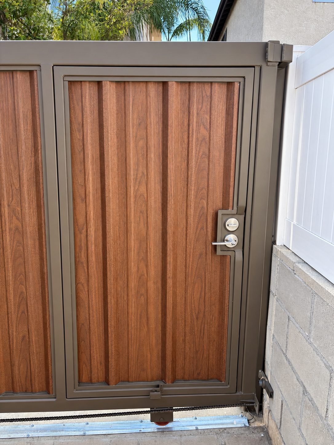 Close-up of pedestrian door built into sliding gate — wood-grain panels, keyed handle, brown steel frame