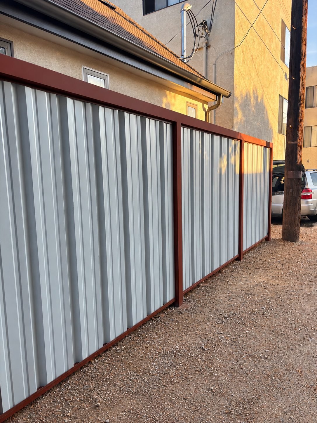 Back view of fence with grey corrugated steel panels and burgundy top rail