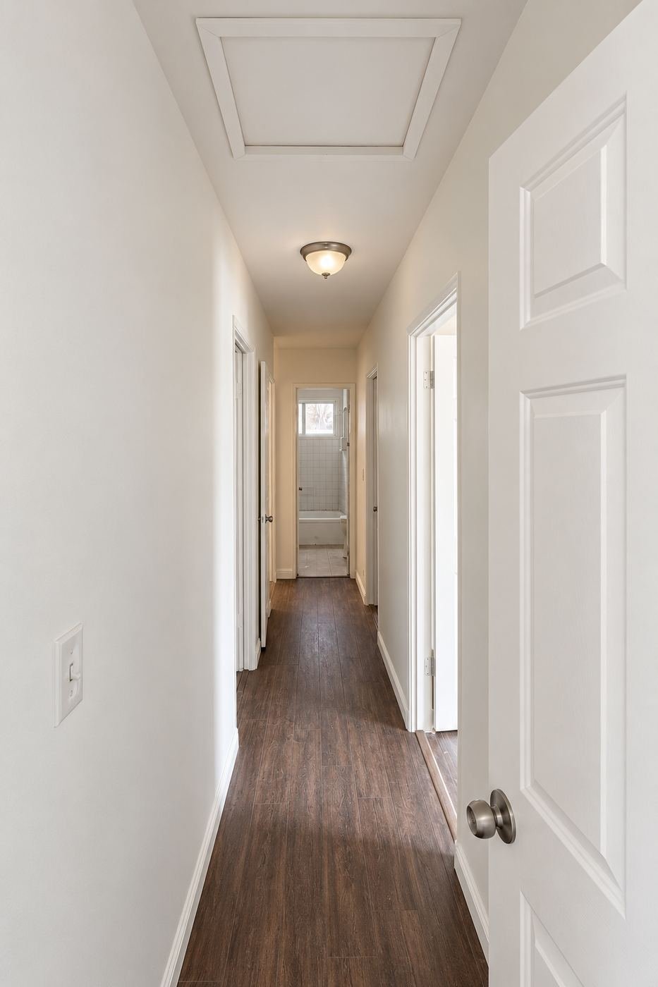 Finished hallway after the Van Nuys water-damage mold remediation and interior repaint — fresh warm-white walls, white ceiling with new flush-mount light, client's dark laminate floor, bathroom at the far end