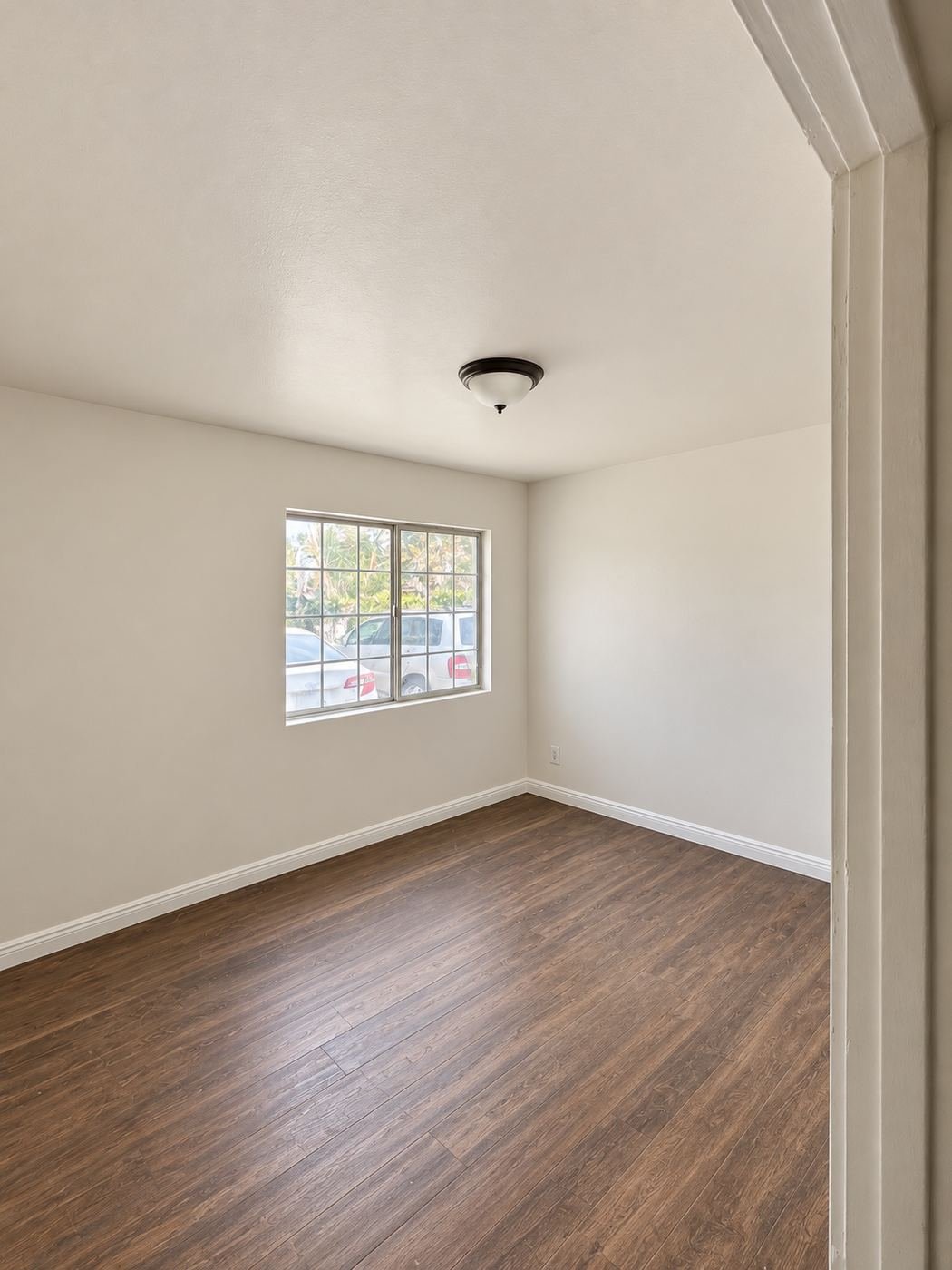 Finished bedroom with a large garden window after the Van Nuys water-damage restoration — warm-white walls, white ceiling with new flush-mount light, client's dark laminate floor cleaned and left in place